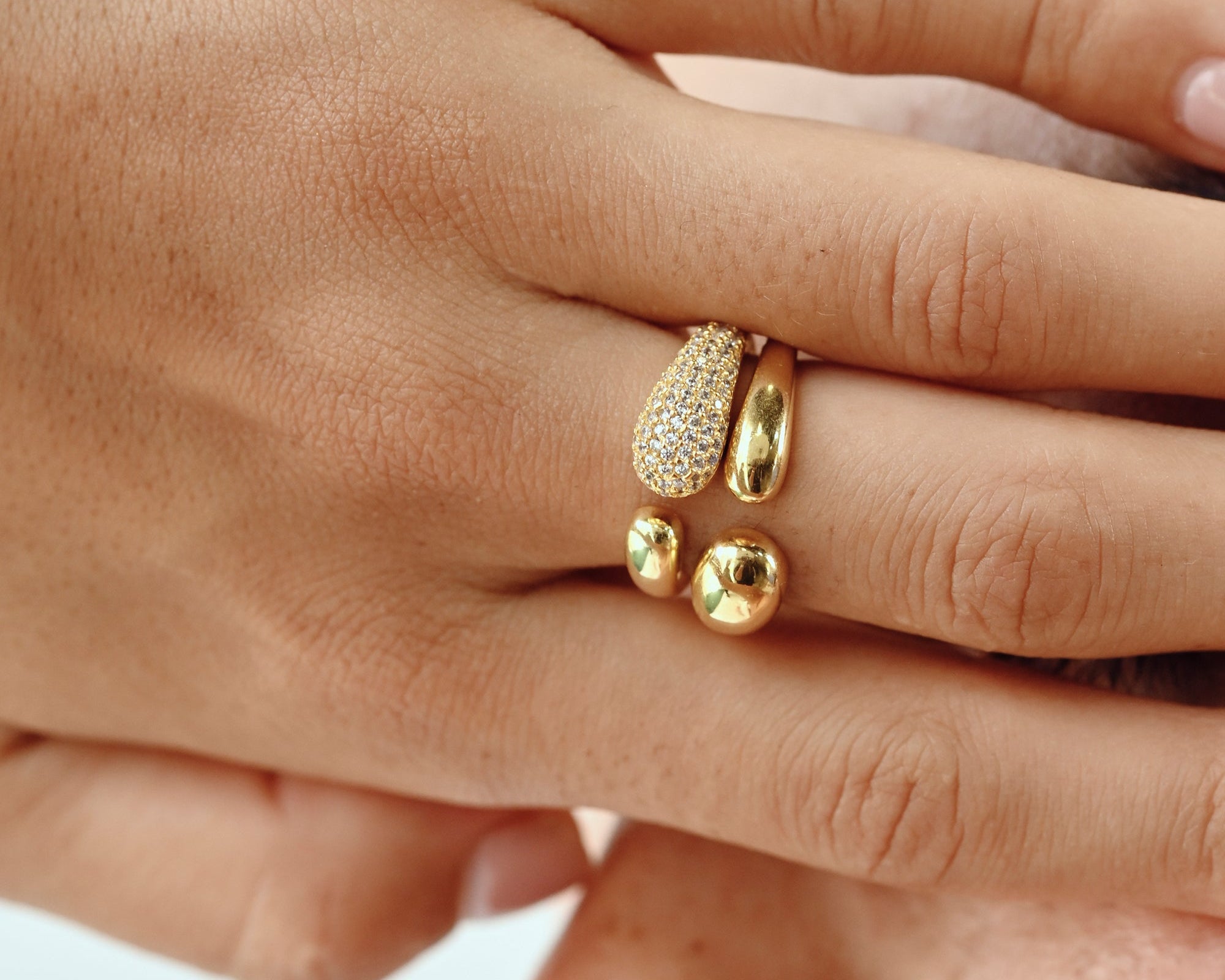 A close-up image of a person's hand showcasing a gold-colored band ring with frosted pebble texture and a central cubic zirconia (CZ).