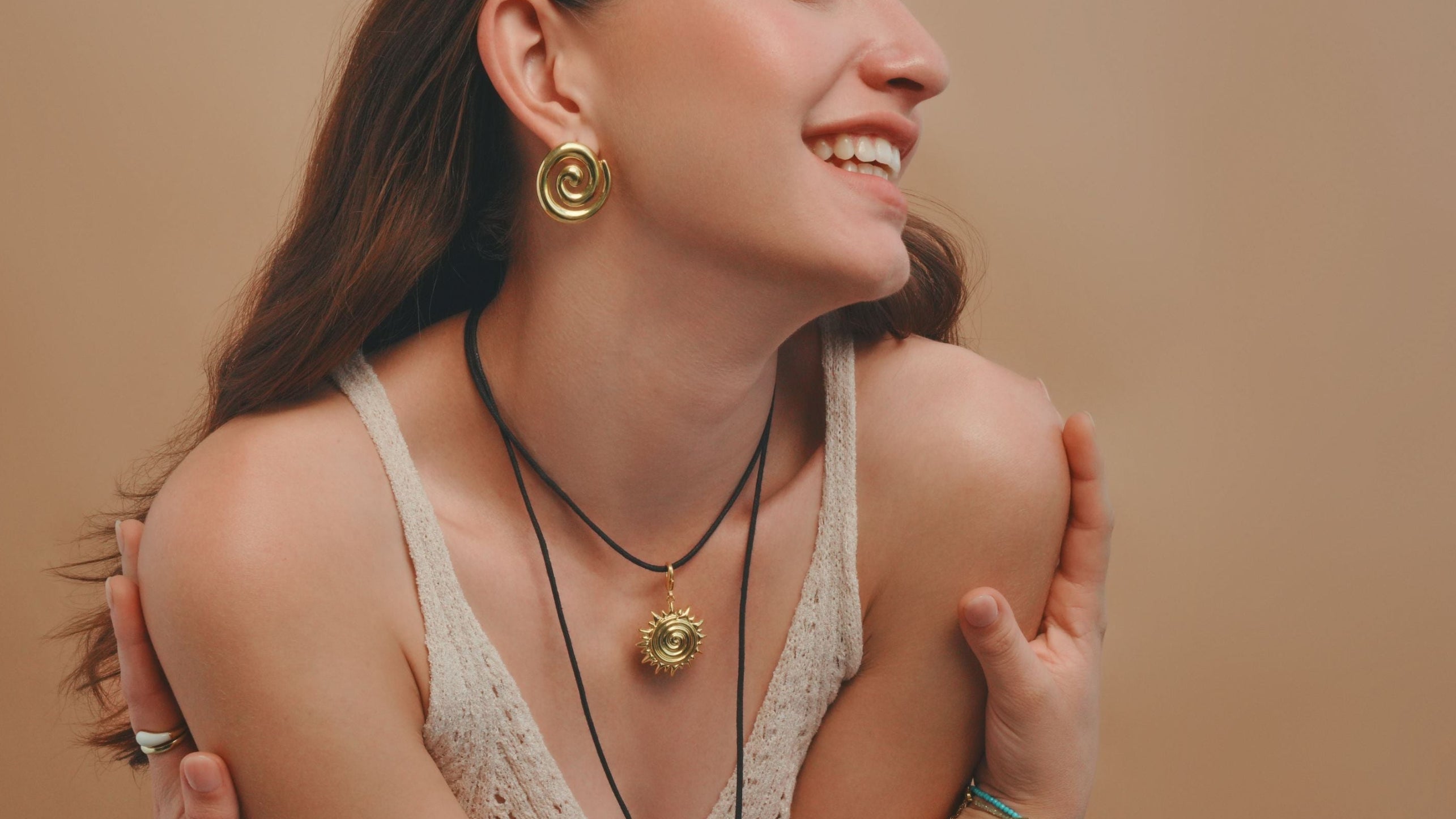 Woman wearing gold necklaces and earrings against a beige background