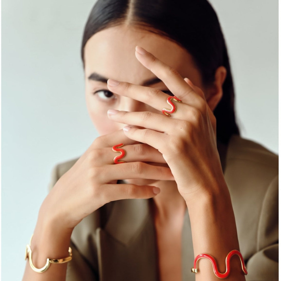 A model wearing a matching pair of bright yellow wavy snake-shaped rings and bracelets, shown in a close-up portrait against a neutral light gray background.