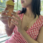 Woman in a red checkered dress holding a small ice cream cone with a yellow top.