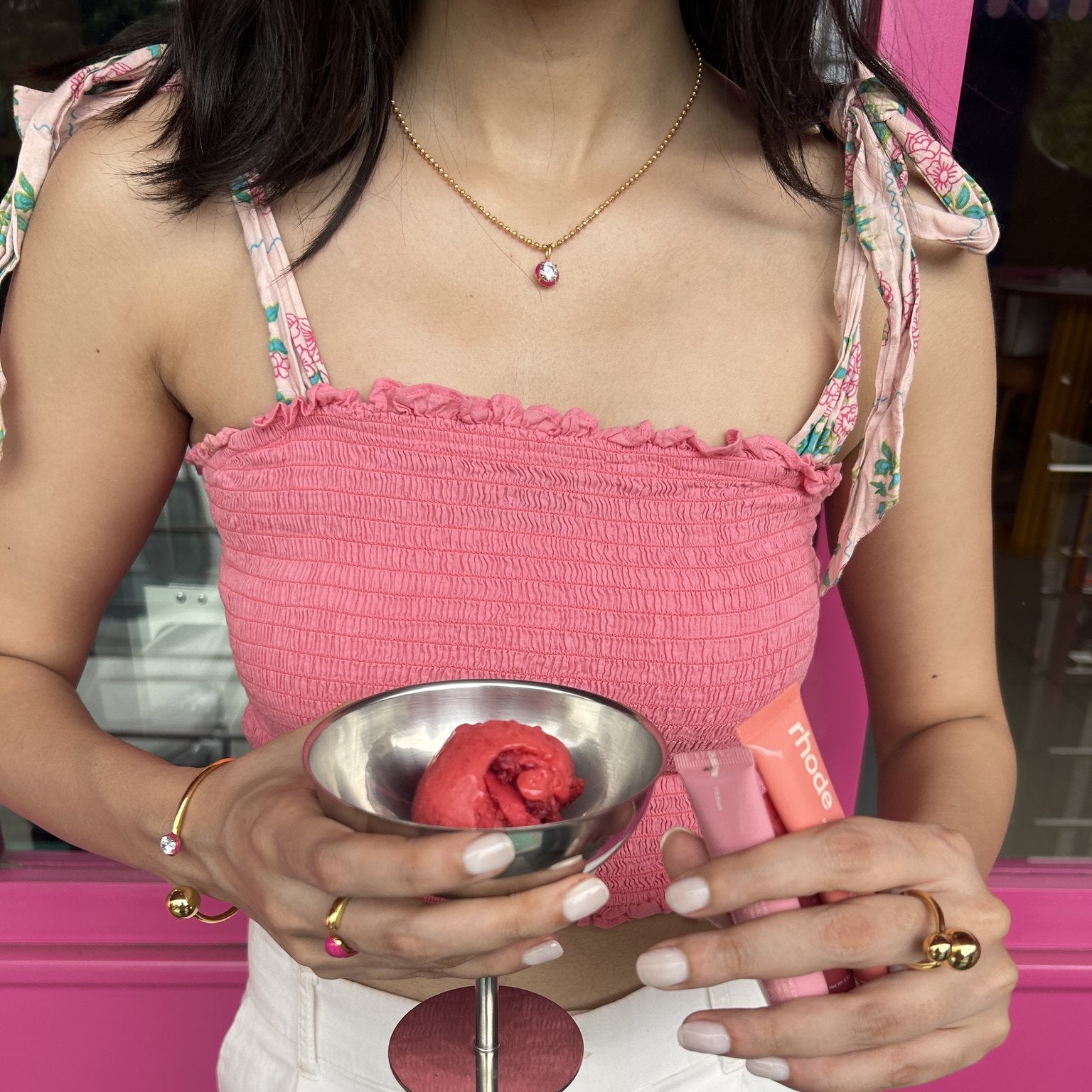 Person holding a small metal bowl with red object against a pink background