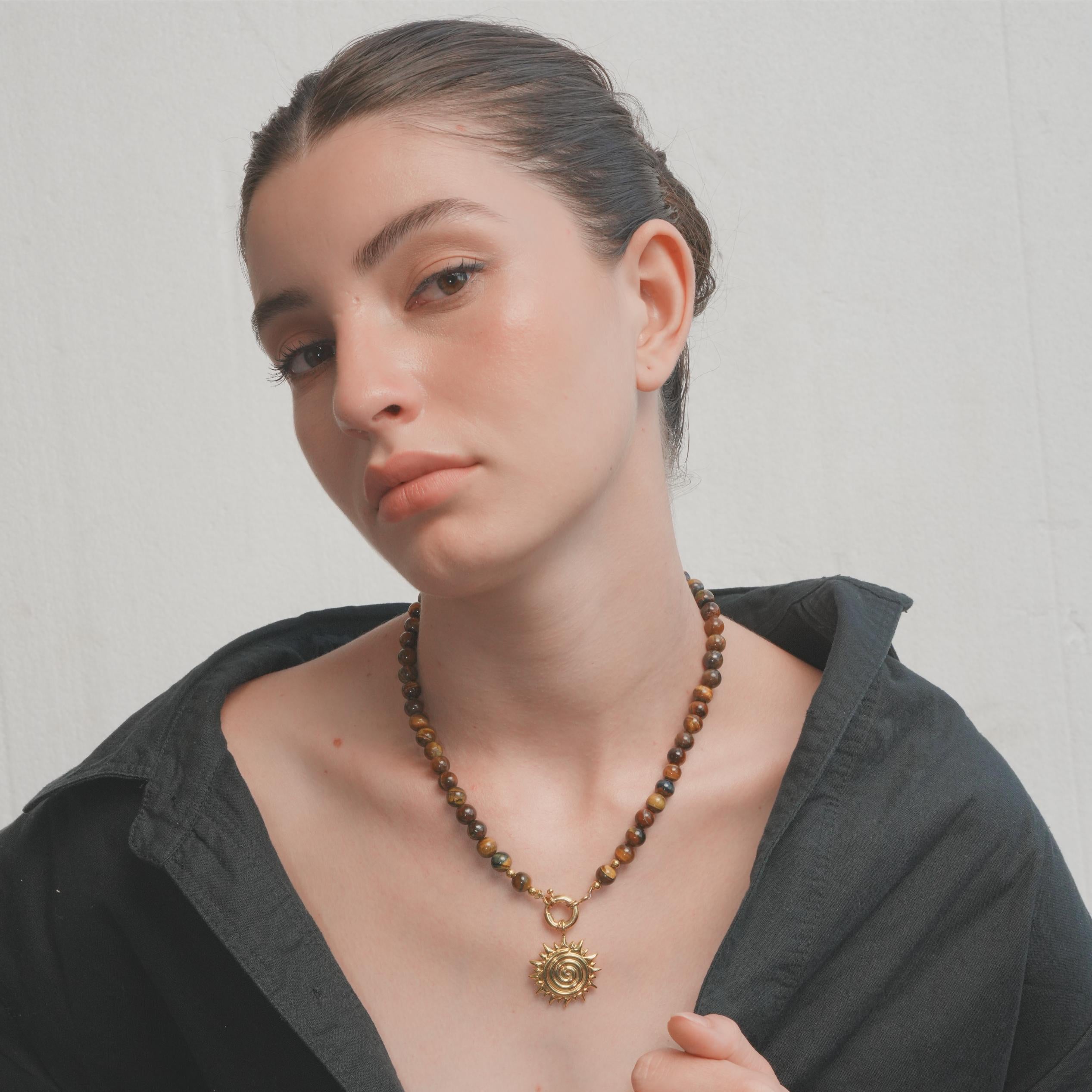 Woman wearing a necklace with a gold pendant against a plain background